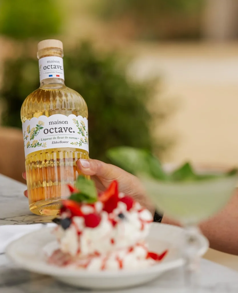 Bouteille Maison Octave tenue en main, avec une pavlova aux fruits rouges en terrasse