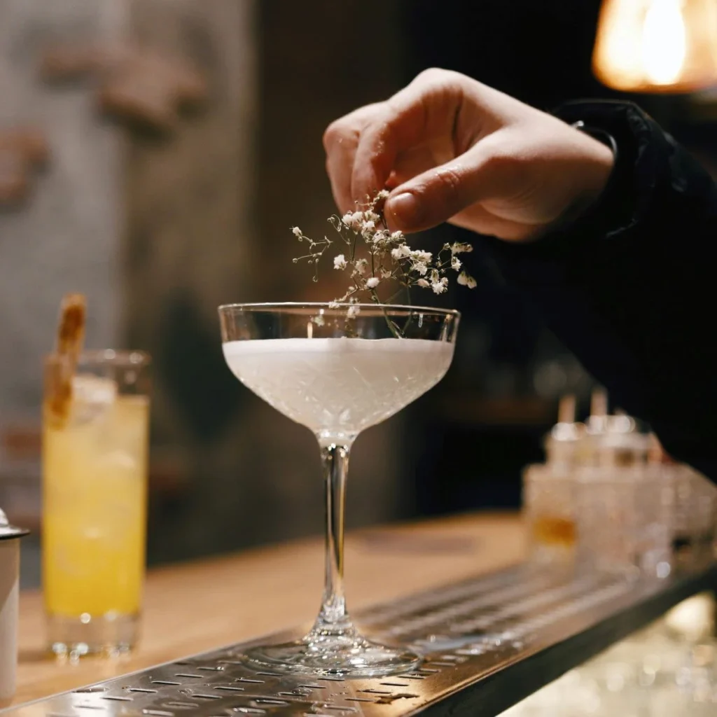 Main de barman déposant une fleur de sureau sur un cocktail